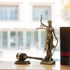 Alegoria sprawiedliwości z wagą i mieczem, obok młotka sędziowskiego i ksiąg prawniczych. Symbol prawa i porządku.
