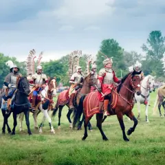 Husaria, żywe polskie mity narodowe, przemierza zielone pola w pełnym rynsztunku.