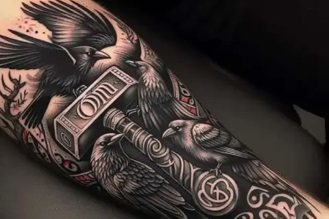 Tatuaż kruka z młotem Thora. Kruki symbolizują mądrość i pamięć, a młot to potęga i ochrona.
