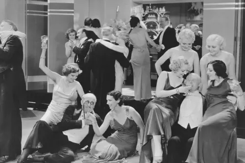 Zabawa towarzyska w stylu dwudziestolecie międzywojenne ramy czasowe. Eleganckie kobiety i mężczyźni w strojach z epoki, toastowanie i tańce.