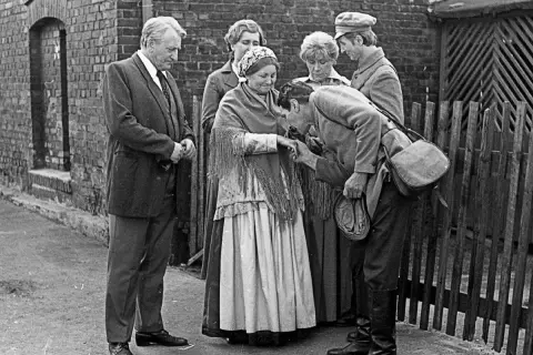 Scena z filmu "Antoni Lulek. Poglądy". Mężczyzna całuje dłoń starszej kobiecie, otoczeni przez innych ludzi.
