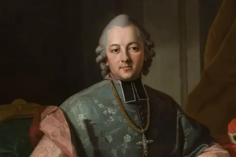 Portret biskupa w stroju duchownym, z łańcuchem i krzyżem. Postać odzwierciedla styl epoki oświecenia, w której tworzył Krasicki.