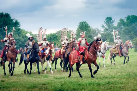 Husaria, żywe polskie mity narodowe, przemierza zielone pola w pełnym rynsztunku.