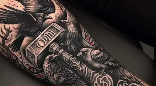 Tatuaż kruka z młotem Thora. Kruki symbolizują mądrość i pamięć, a młot to potęga i ochrona.