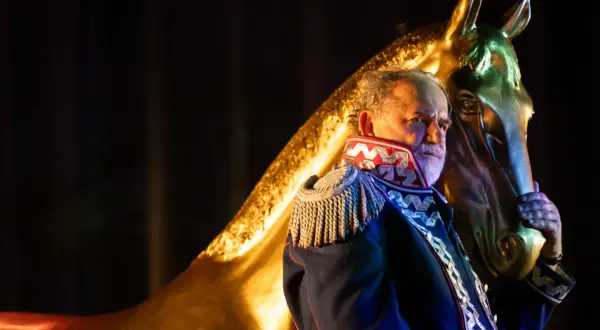 Starszy mężczyzna w mundurze, jak z epilogu "Pana Tadeusza", trzyma złotą głowę konia.